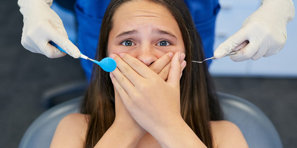 A young woman covers her mouth with a look of fear while visiting the dentist due to dental anxiety