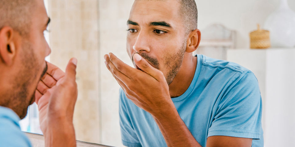 What causes bad breath? A man checked his breath in the mirror
